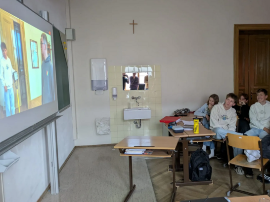 Schüler:innen sitzen in einem Klassenraum und sehen gemeinsam eine auf die Tafel projizierte Videoaufnahme.