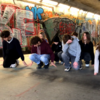 Videostill tanzende Schülerinnen und Schüler unter einer Brücke mit Graffiti im Hintergrund