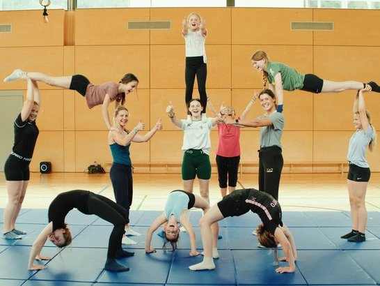 Mehrere Kinder tanzen und machen Turnübungen in einer Sporthalle