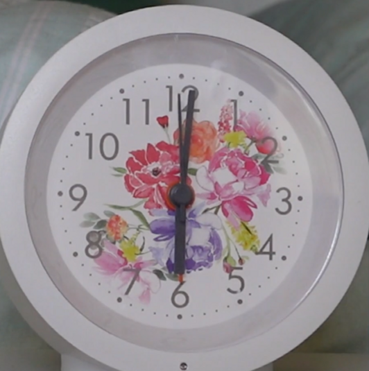 Videostill eines Weckers weiß mit roten, rosa, lila Blumen