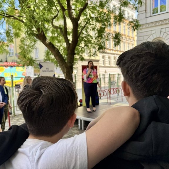 Schüler:innen verfolgen gemeinsam eine Bühnenpräsentation im Freien im Rahmen der Klima Biennale Wien.