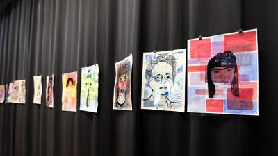 Das Bild zeigt aufgehängte Bilder vor einem schwarzen Vorhang