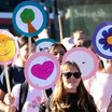 Schüler:innen bei einer Aktion im öffentlichen Raum mit selbst gestalteten, bunten Schildern mit Symbolen wie Smiley, Baum, Herz und Blume.