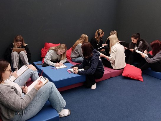 Eine Gruppe von Schülerinnen sitzen in einem Raum und machen Notizen.