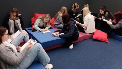 Eine Gruppe von Schülerinnen sitzen in einem Raum und machen Notizen.