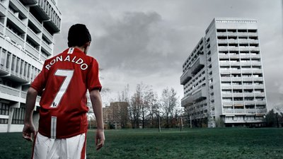 Jugendlicher im roten Fußballtrikot auf einer Wiese vor Wohnhäusern