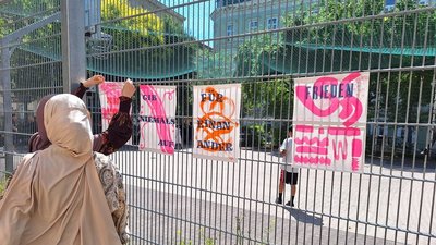 Personen befestigen selbst gestaltete Plakate zum Thema Frieden an einem Zaun.