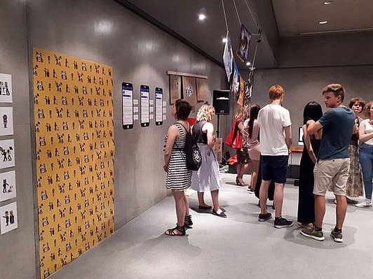 Mehrere Jugendliche in einem Museum. Manche lesen sich Informationen durch, während andre in Gruppen sich Ausstellungsstücke ansehen.