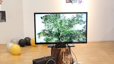Medieninstallation mit Bildschirm, Radio, Zeitungen und Luftballons.