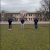 Videostill mit 3 Schülern auf deiner Wiese mit der Schule im Hintergrund