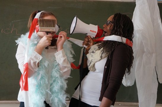 Zwei Schülerinnen gestalten eine performative Szene mit Megafon, Pinsel und Absperrband im Rahmen eines Kulturvermittlungsprojekts.