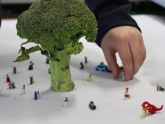 Ein Brokkoli auf einem weißen Tisch mit kleinen Spielzeugfiguren