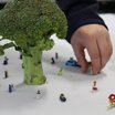Ein Brokkoli auf einem weißen Tisch mit kleinen Spielzeugfiguren