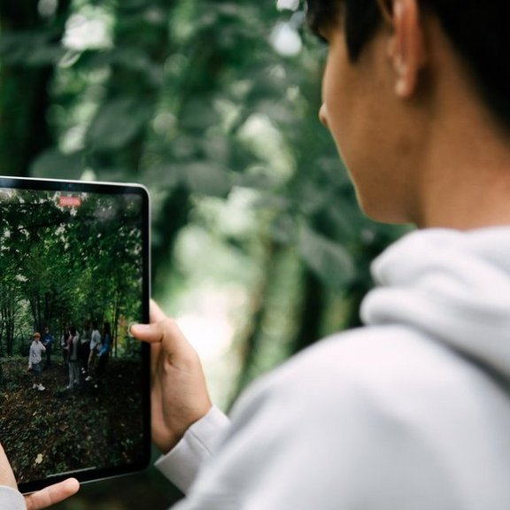 Junger Mann mit Tablet macht ein Foto von einer Gruppe Jugendliche im Wald