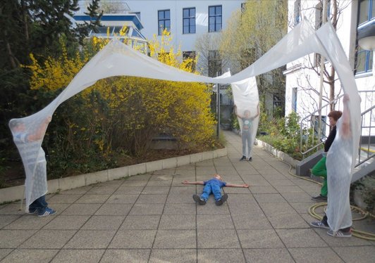 Foto von SchülerInnen, die mit Stoffbahnen im Schulhof „Räume‟ aufspannen