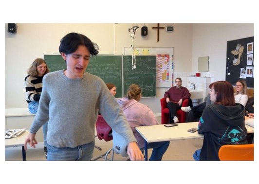 Bild von mehreren Jugendlichen einige sitzend einer geht weg mit einem verzerrten Gesicht. 