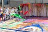 Kinder in weißen Malerkitteln schütten in einer malaktion Farbe auf eine große Leinwand.