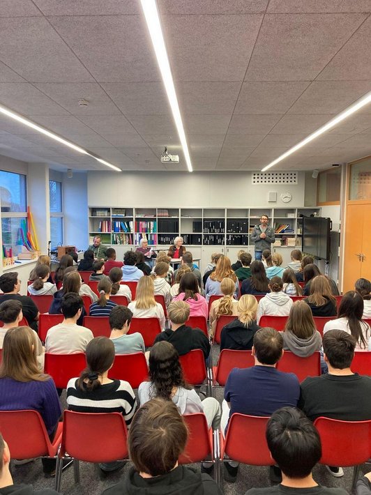Schüler/innen sitzen in Sesselreihen vor zwei Zeitzeuginnen und zwei Männern
