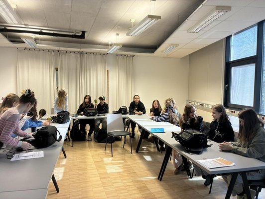 Foto von Schüler:innen sitzend um Tische in Zweier-Teams mit Interview Equipment.