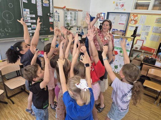 Kindergruppe mit hochgestreckten Händen in Klassenzimmer neben Frau, die kleine Lampe hält