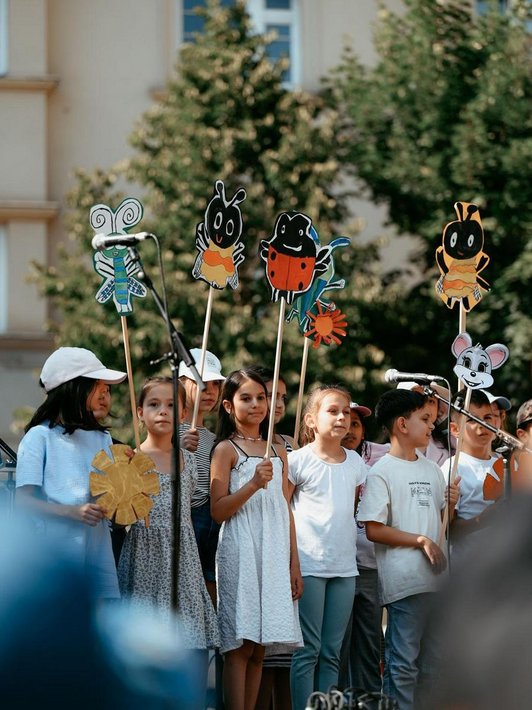Schüler/innen halten gezeichnete Insekten auf Stecken in die Luft