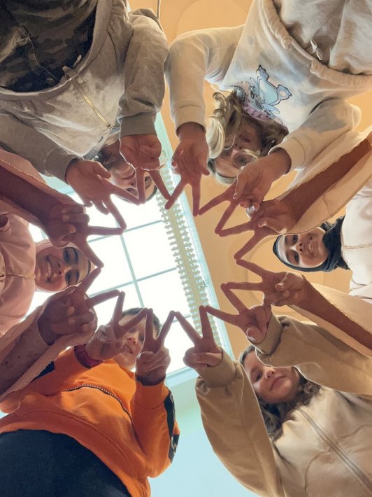 Foto von unten aufgenommen, Jugendlichen die in einem Kreis stehen und die Finger in V Form zusammenhalten.