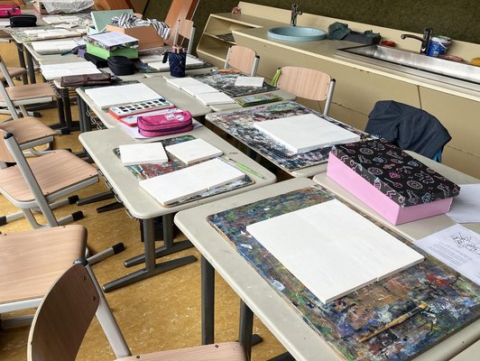 Foto von Schülertischen mit leeren Leinwänden darauf und Malkästen.
