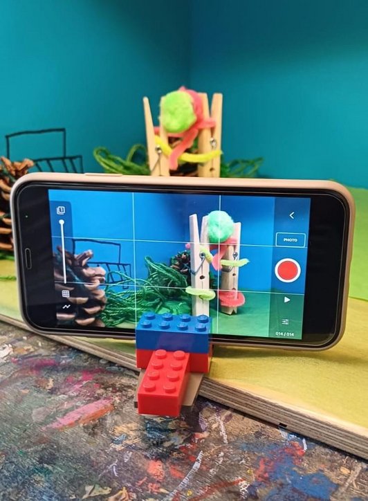 Handy steht auf einer Legostützen und filmt eine Filmszene mit zwei Wäscheklammern.