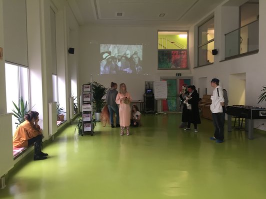 Foto von der Performance der Schüler/innen im Schulgebäude mit Videoprojektion im Hintergrund