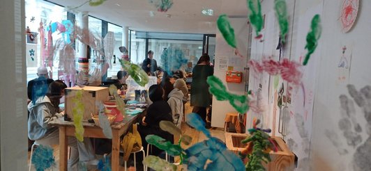 Arbeitsraum mit Schüler/innen fotografiert durch Glas voller bunter Handabdrücke