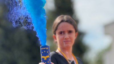 Foto einer Schülerin die einen Energydrink mit dem Zeichen der Europäischen Union hält, aus dem blauer Rauch aufsteigt