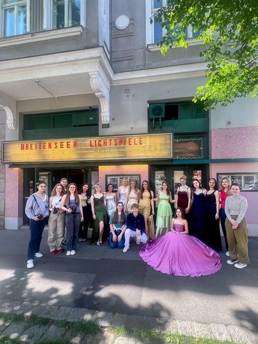 Gruppenbild von Schulklasse vor Kino-Eingang, ein Mädchen in violettem Ballkleid