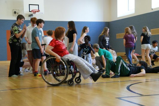 mehrere Schüler/innen in einem Turnsaal, Frau in Rollstuhl im Vordergrund