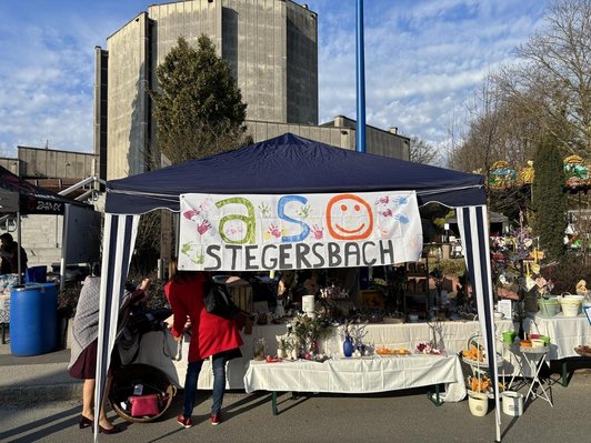 Foto von einem Zelt mit einem Banner "ASO Stegersbach"Auf einem Tisch stehen selbstgemachte Ostersachen.