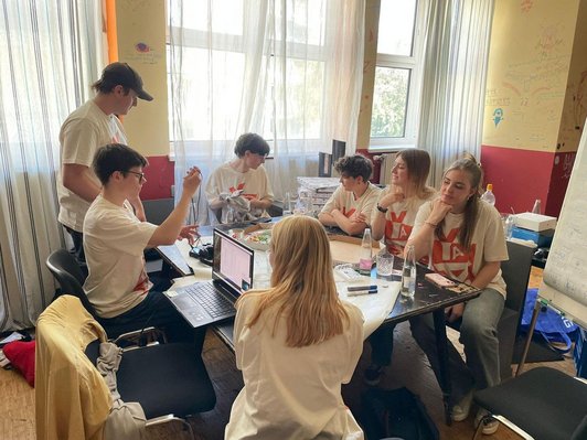 Jugendliche sitzen um Tisch mit Laptop, Flipcharts, Markern und Pizza