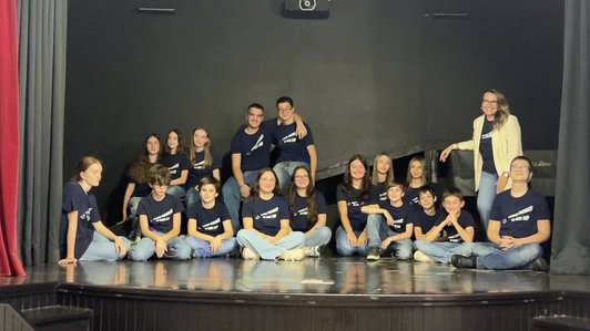 Eine Gruppe von Schüler:innen sitzend auf einer Bühne. Alle mit einheitlicher Kleidung.