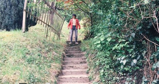 Videostill von einem Schüler, der auf einer Stiege im Grünen steht