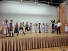 Kinder in Lederhosen und Dirndl tanzen auf einer Bühne.