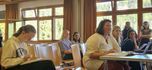 Foto in eriner Klasse von Schülerinnen und einer Lehrperson mit einem Laptop.