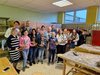 Foto von Schüler/innen und Lehern und Großeltern in einem Werksaal.Sie halten selbstgemachte Objekte aus Weide in ihren Händen