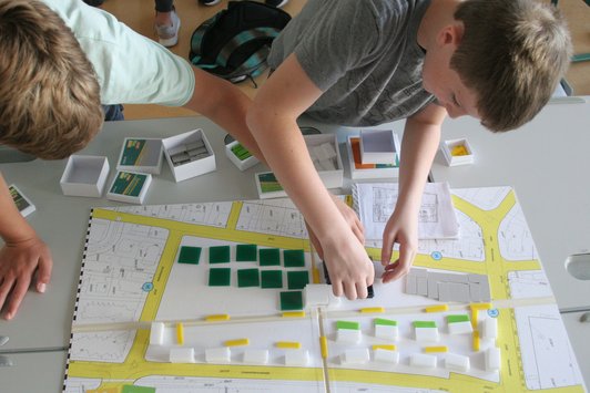 Foto von zwei Schülern, die Spielmaterial auf den Stadtspielplan legen