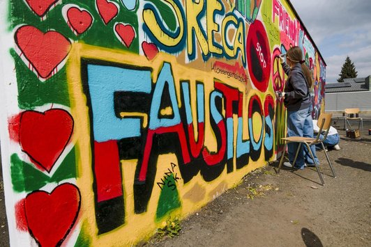 Bunte Wand im Schulhof, die mit Sprüchen und Symbolen gerade von zwei Schüler/innen besprüht wird.