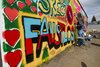 Bunte Wand im Schulhof, die mit Sprüchen und Symbolen gerade von zwei Schüler/innen besprüht wird.
