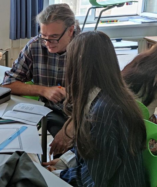 Mädchen und Mann sitzen an Tisch und blicken auf Papierblatt