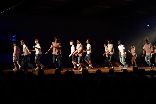 Schüler/innen in Tanzpose auf Bühne, Publikum im Vordergrund