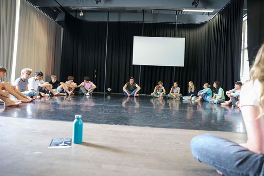 Schüler/innen und Mann sitzen am Boden im Kreis