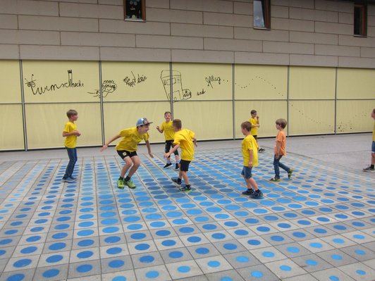 Foto von sieben Schülern beim Spielen im von ihnen mit blauen Punkten gestalteten Schulhof