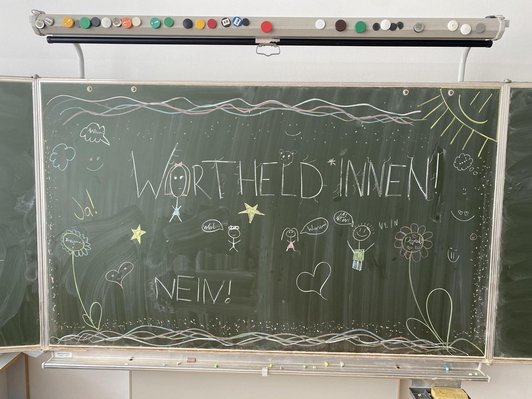 Auf einer Schultafel steht mit Kreide geschrieben "Wortheldinnen! Nein"