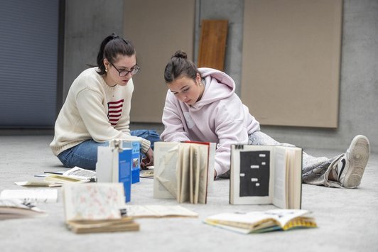 Zwei Schüler/innen gestalten am Boden ihre Büche, die vor ihnen liegen