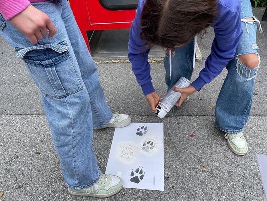 zwei Jugendliche sprühen mit Schablone Tierspuren  auf Gehsteig